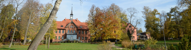 Verwaltungsgebäude des SKH Altscherbitz, Außenansicht, im Vordergrund herbstlicher Park mit Wiese und Bäumen